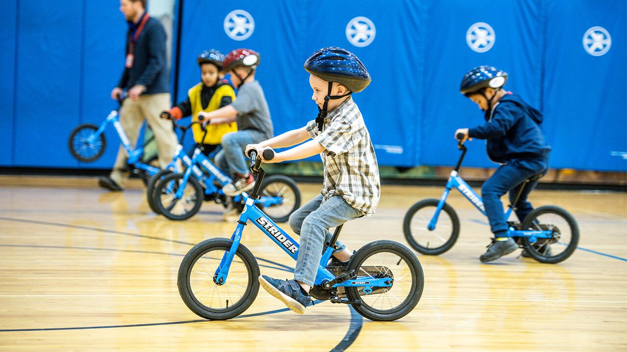 A boy rides a blue Strider bike in a gymnasium